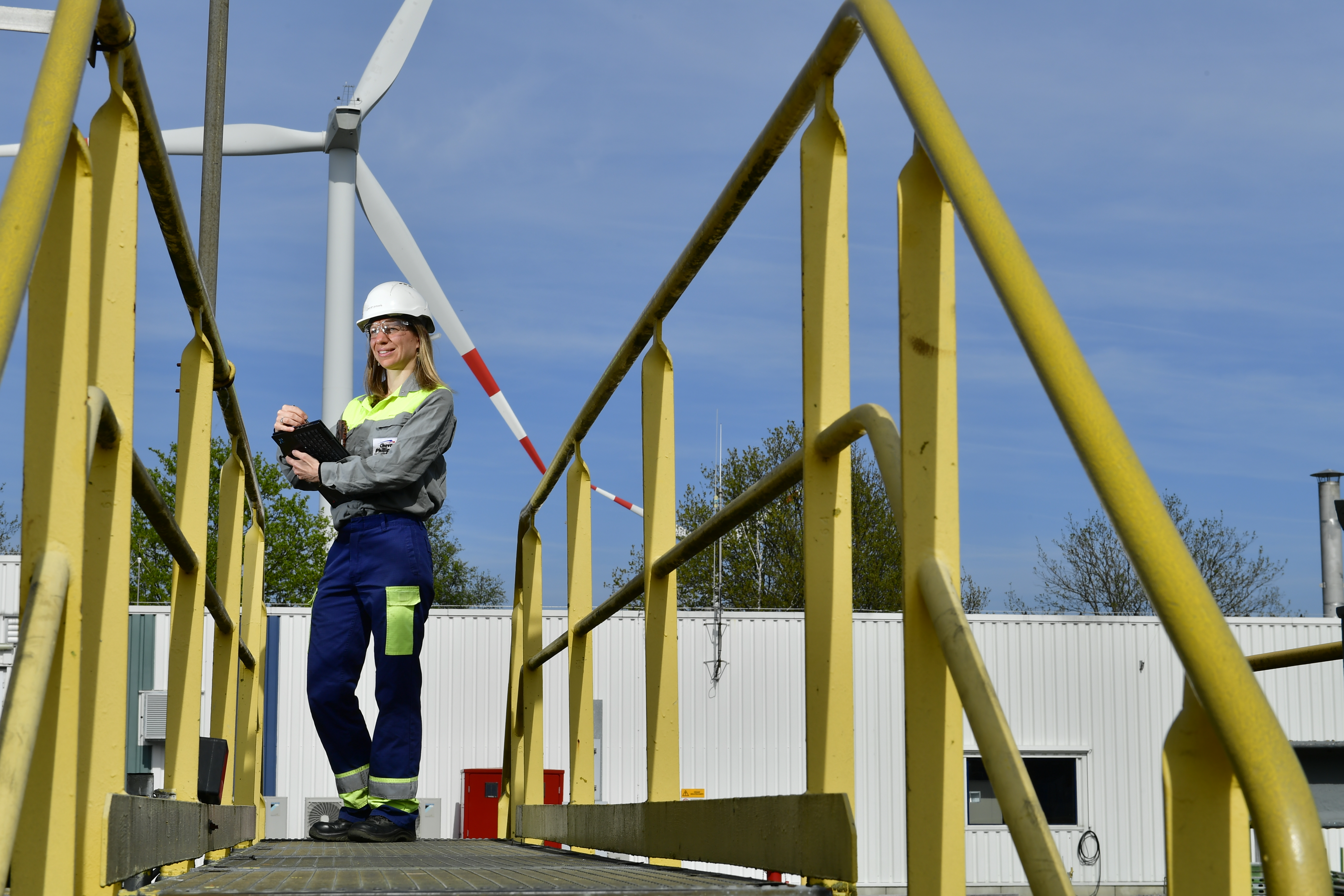 Employee with safety gear and a clipboard with wind turbine in the background