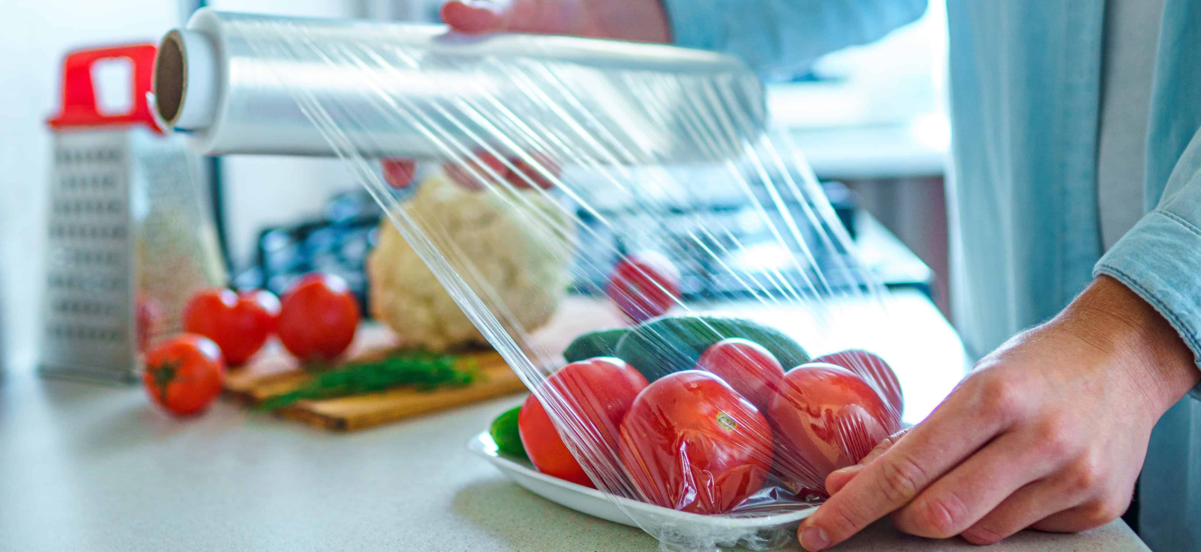 person wraps tomatoes in plastic wrap