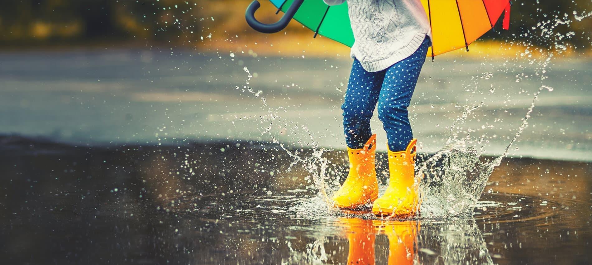 Child wearing rain boots jumping in a puddle with an umbrella